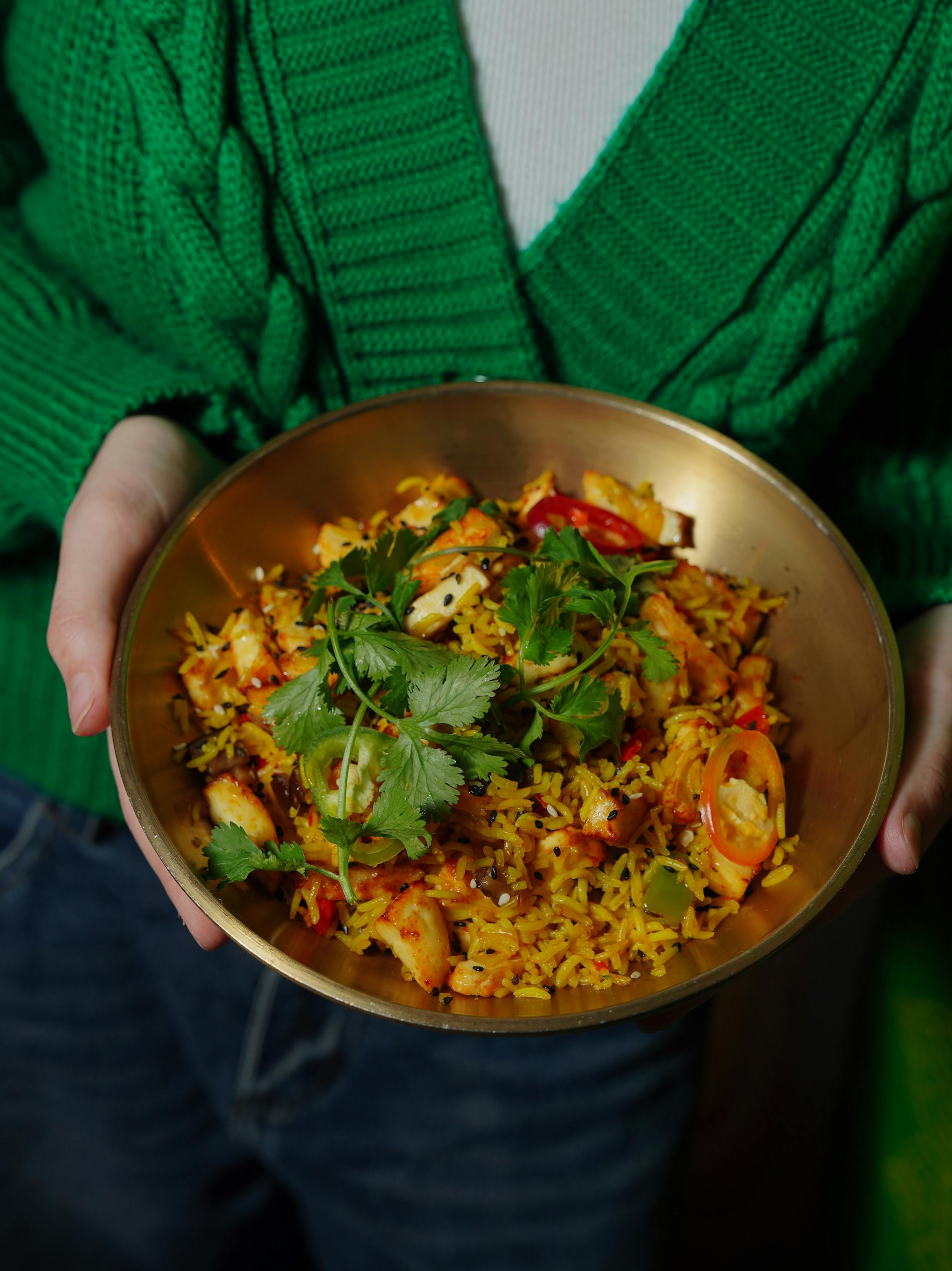 Vibrant rice dish held by a person in a green sweater, garnished with cilantro and fresh vegetables.
