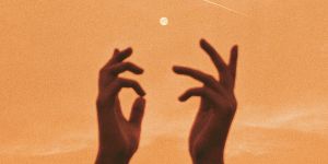 Silhouetted hands reaching up towards the moon and a shooting star in a warm orange sky.